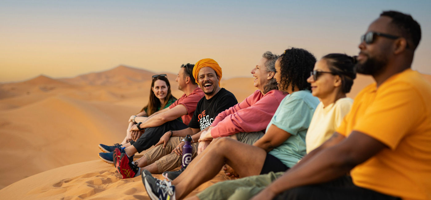 Image: A G Adventures group CEO and travelers sit in the sand dunes in Morocco. (Photo Credit: G Adventures)