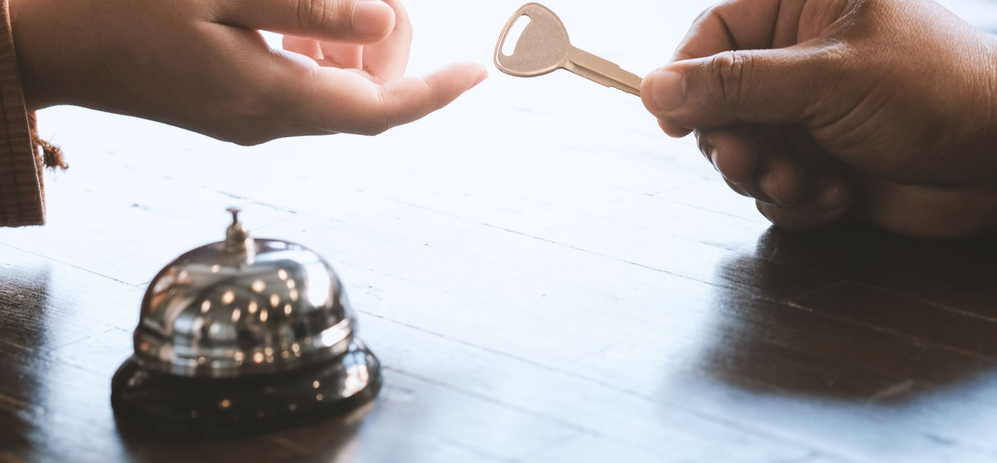 Image: Guest checking in at a hotel front desk. (Photo Credit: Adobe Stock/Charlie's)