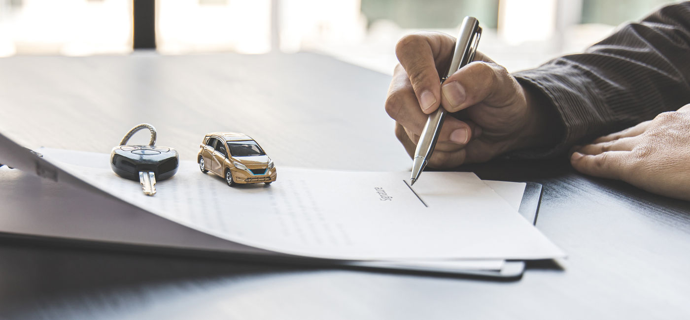 Image: Traveler signing a rental car agreement. (Photo Credit: Puwasit Inyavileart/Adobe)