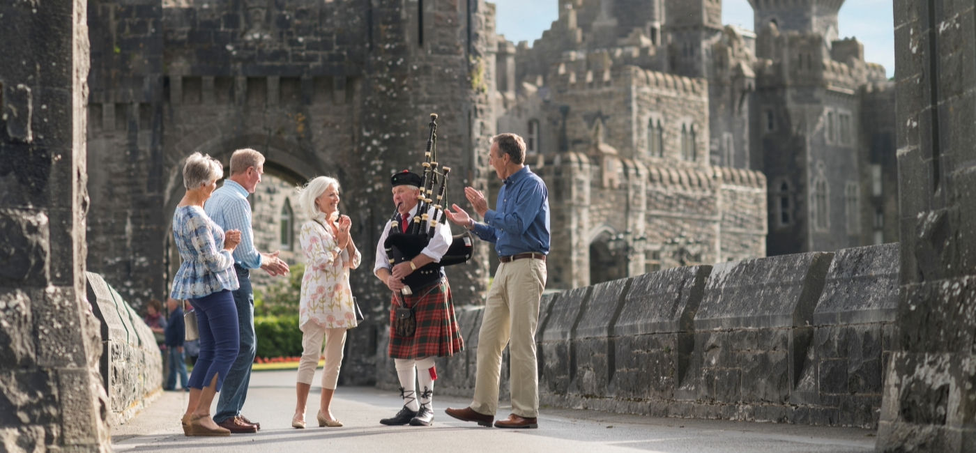 Image: Travelers listen to a bagpipe player at Ashford Castle in Cong, Ireland. (Photo Credit: TTC Tour Brands)