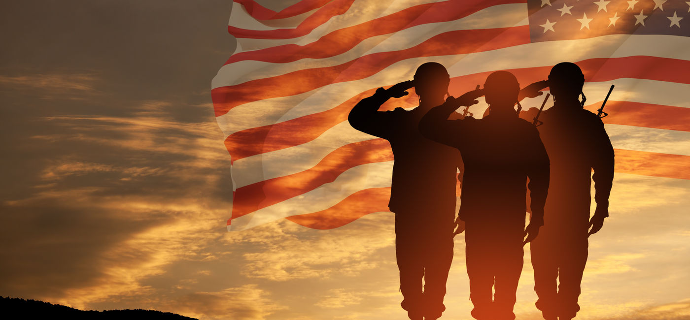 Image: US Army soldiers saluting with an American flag in the background. (Photo Credit: Adobe Stock/hamara)