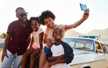 Family posing for selfie next to car packed for road trip.