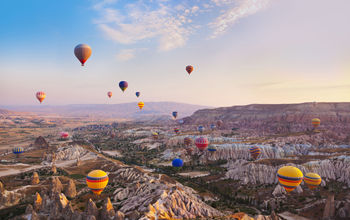 Hot air balloon flying over rock landscape at Cappadocia Turkey (photo via TPopova / iStock / Getty Images Plus)