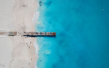 Drone photo of pier in Grace Bay, Providenciales, Turks and Caicos. The caribbean blue sea and white sandy beaches can be seen (photo via JoaoBarcelos / iStock / Getty Images Plus)